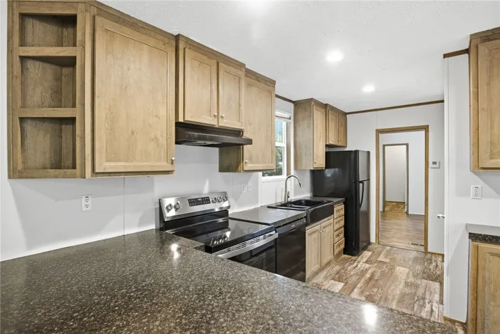 A well-appointed kitchen features dark granite counters, wood cabinets, and modern black appliances.