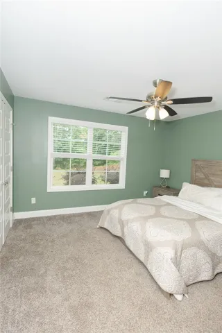 A restful bedroom with ample natural light, soft carpeting, and a modern ceiling fan.