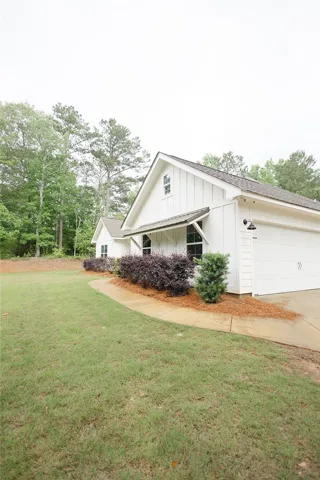 Board and batten siding defines this charming home with an attached garage, surrounded by verdant trees.