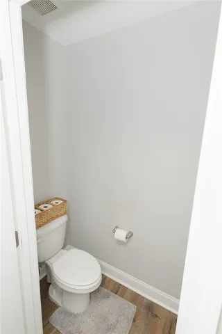 A compact, clean powder room with rich hardwood-style flooring and a simple toilet setup.