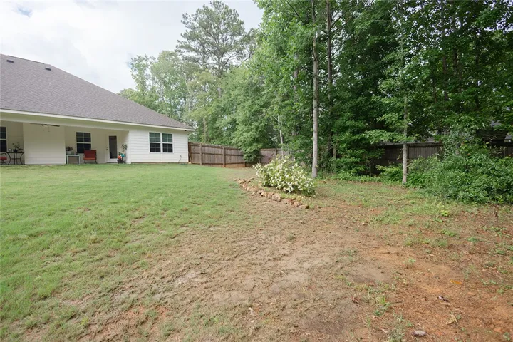A spacious yard extends from the modern white siding, bordered by a wooden fence and mature trees.