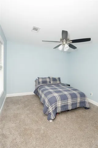 A well-lit bedroom features plush carpeting and a modern ceiling fan for ultimate comfort.