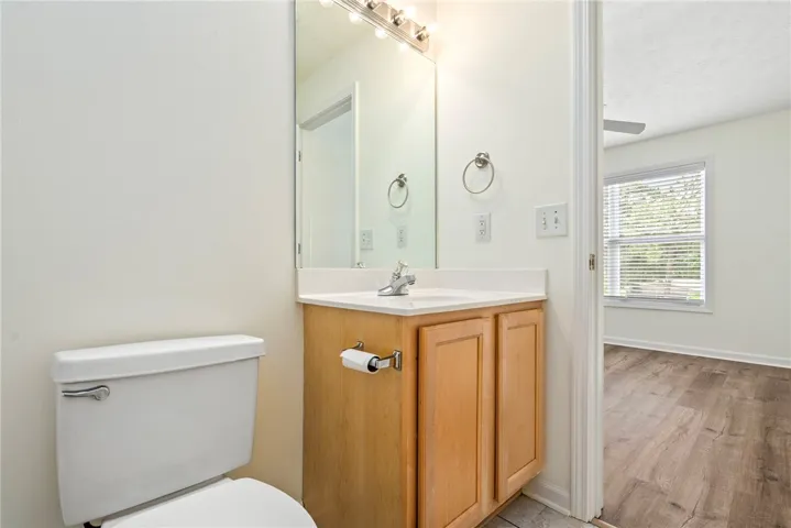 A bright bathroom with a vanity, mirror, and white toilet, offering a peek into an adjacent room.