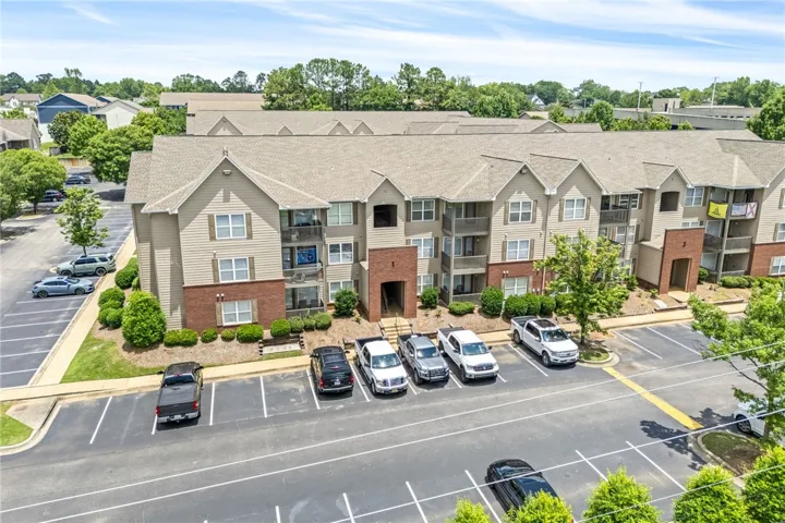 Multi-story residential building with private balconies and ample surface parking.