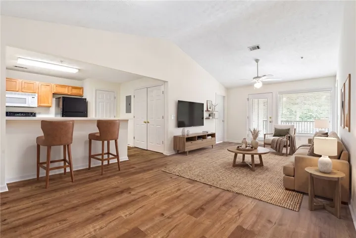 An inviting open-concept living area with soaring vaulted ceilings and rich wood flooring flows into a well-appointed kitchen.