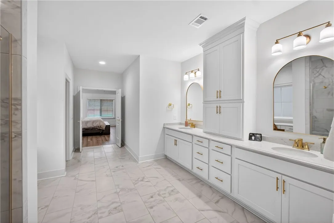 Dual vanity with elegant gold fixtures and a built-in storage cabinet provide convenience and style.