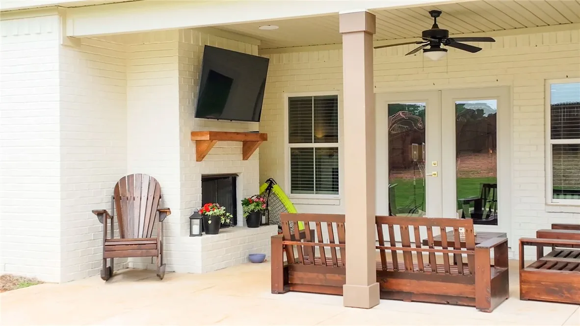 A welcoming outdoor living space features a fireplace, ceiling fan, and access to the verdant yard.