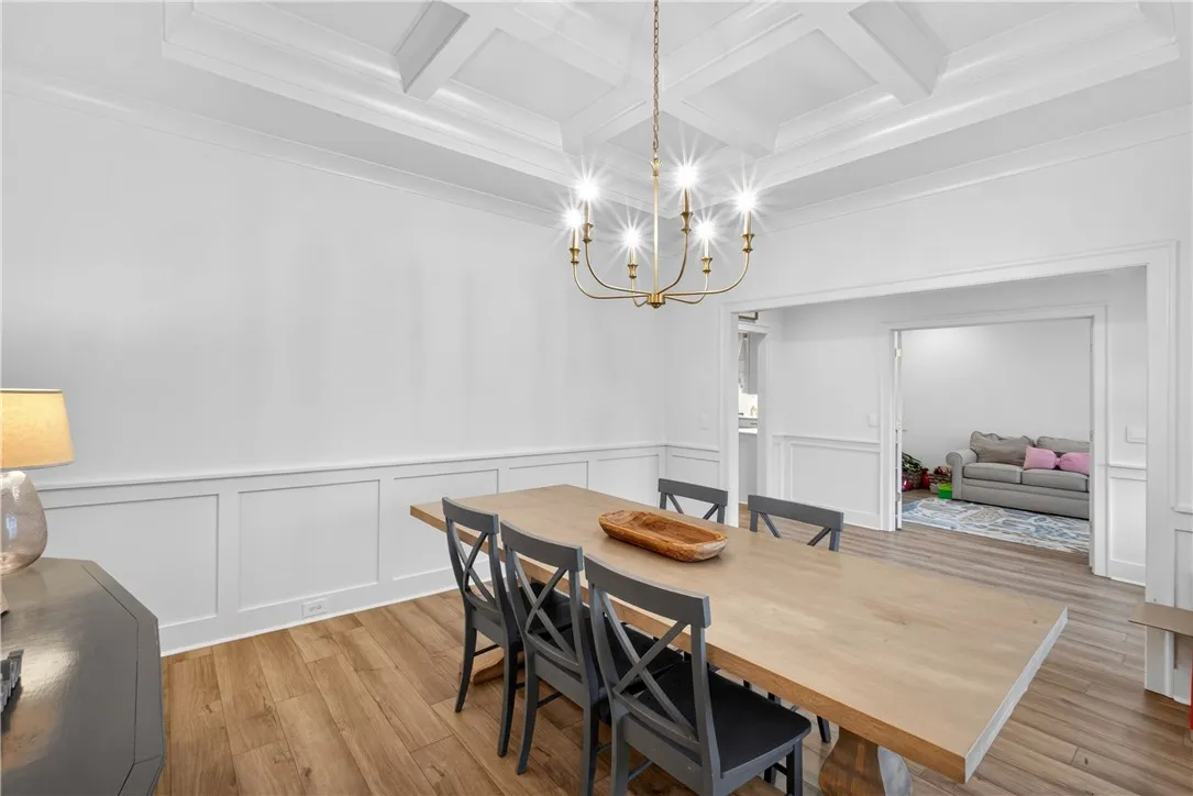 A well-lit dining room features wainscoting and a beautiful coffered ceiling, enhancing its architectural appeal.