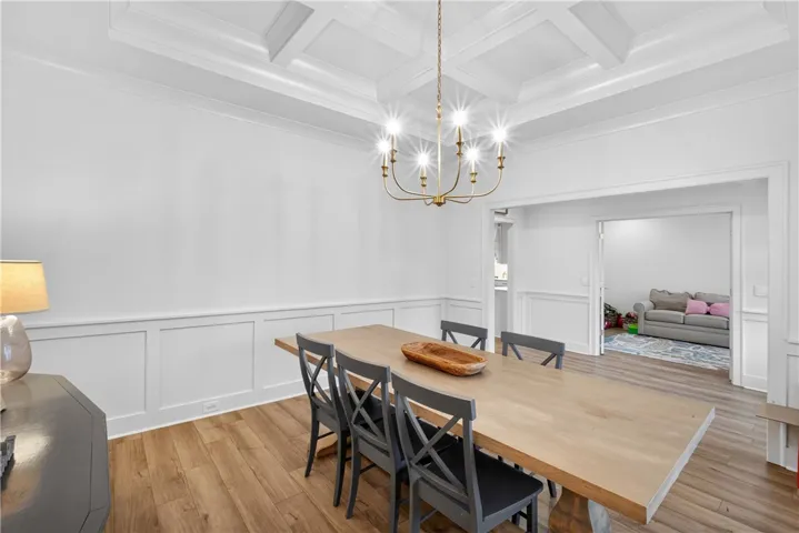 A well-lit dining room features wainscoting and a beautiful coffered ceiling, enhancing its architectural appeal.