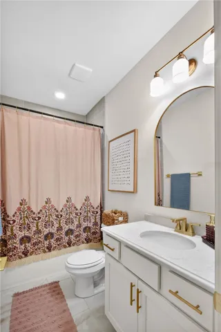 A well-appointed bathroom features a modern vanity with a beveled quartz countertop and gold hardware, complementing the ceramic tile shower surround and flooring.