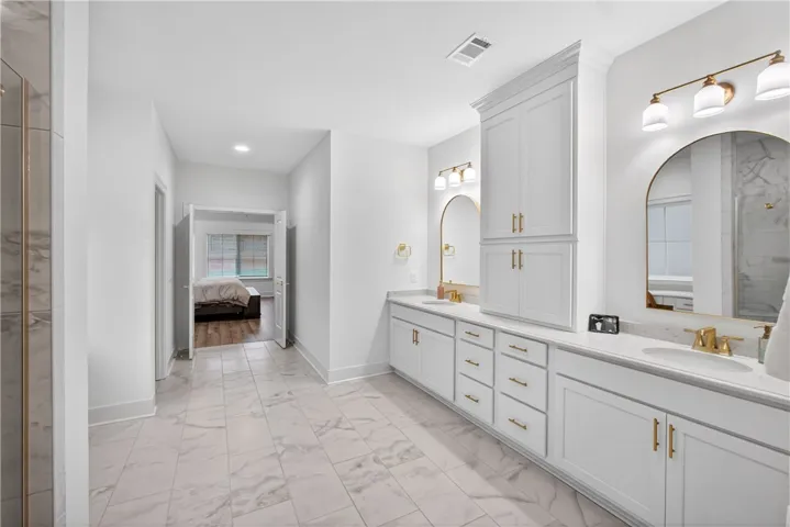 Dual vanity with elegant gold fixtures and a built-in storage cabinet provide convenience and style.