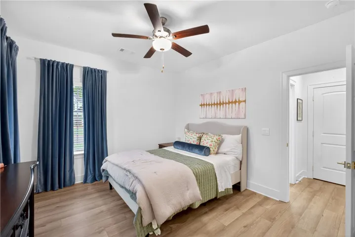 Well-lit bedroom with a ceiling fan, LVP flooring, and bright windows.