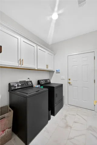 Functional laundry room offers upper cabinetry for storage and easy-care ceramic tile flooring.