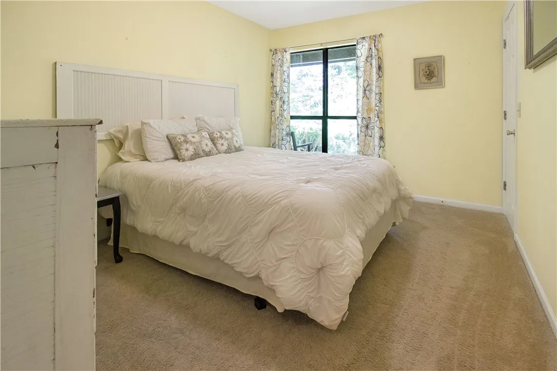 A well-lit sleeping sanctuary features plush carpeting and a serene window view of surrounding greenery.