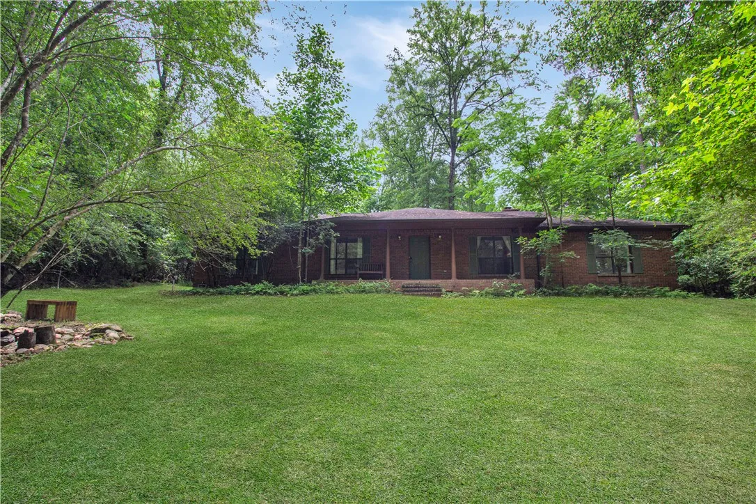 Mature trees surround this brick home with a welcoming front porch and verdant lawn.