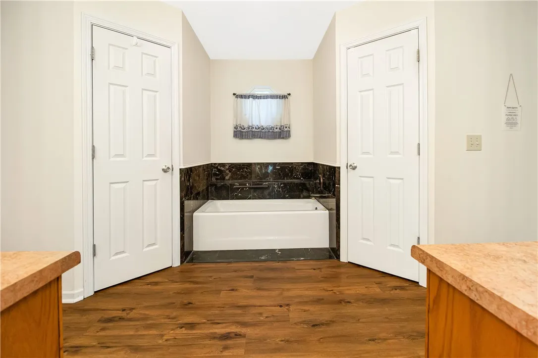 A well-appointed bathroom features a bathtub framed by elegant dark tile and rich wood flooring.