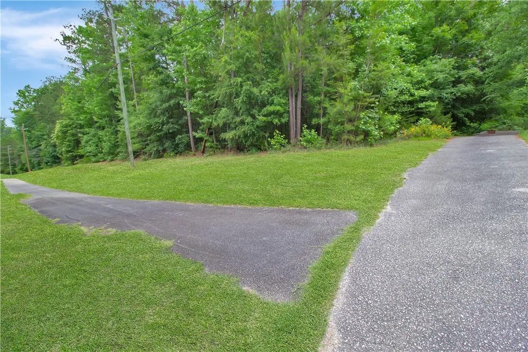 Green landscaping and a paved drive lead to a wooded property. Sidewalks from driveway for biking/jogging