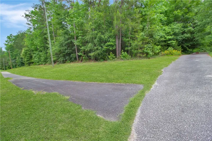 Green landscaping and a paved drive lead to a wooded property. Sidewalks from driveway for biking/jogging