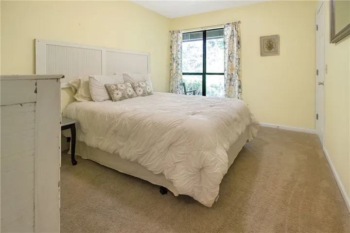 A well-lit sleeping sanctuary features plush carpeting and a serene window view of surrounding greenery.