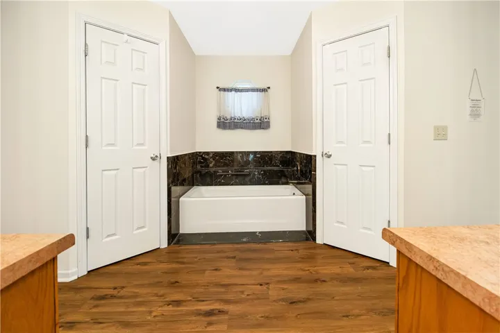 A well-appointed bathroom features a bathtub framed by elegant dark tile and rich wood flooring.