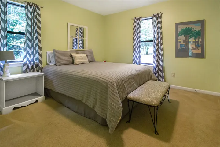 A tranquil bedroom features warm carpeting and ample natural light through well-dressed windows.