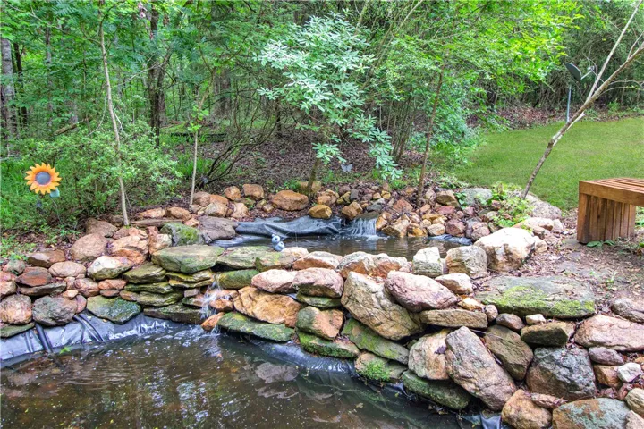 A tranquil backyard oasis features a natural rock-lined pond with cascading water surrounded by lush greenery.
