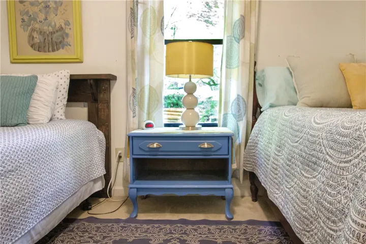 A comforting bedroom setup features two beds with intricate bedspreads, flanking a quaint nightstand with a lamp.