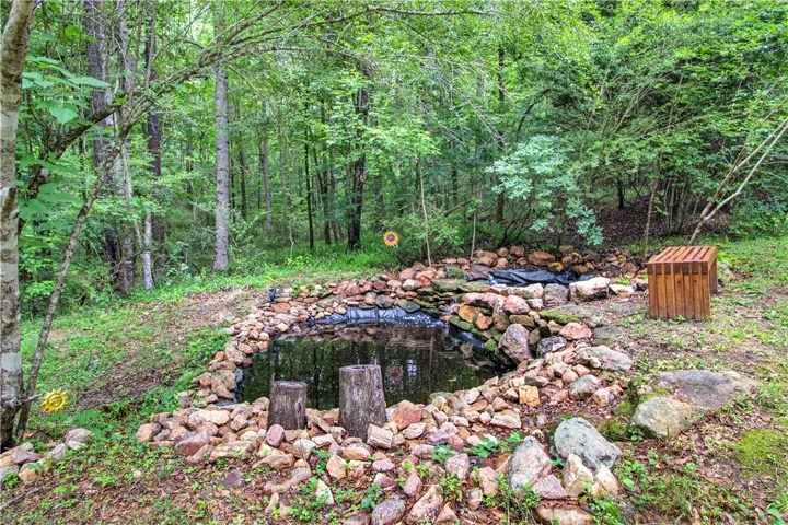 A tranquil pond with rock-lined edges provides a serene, natural retreat within this wooded property.