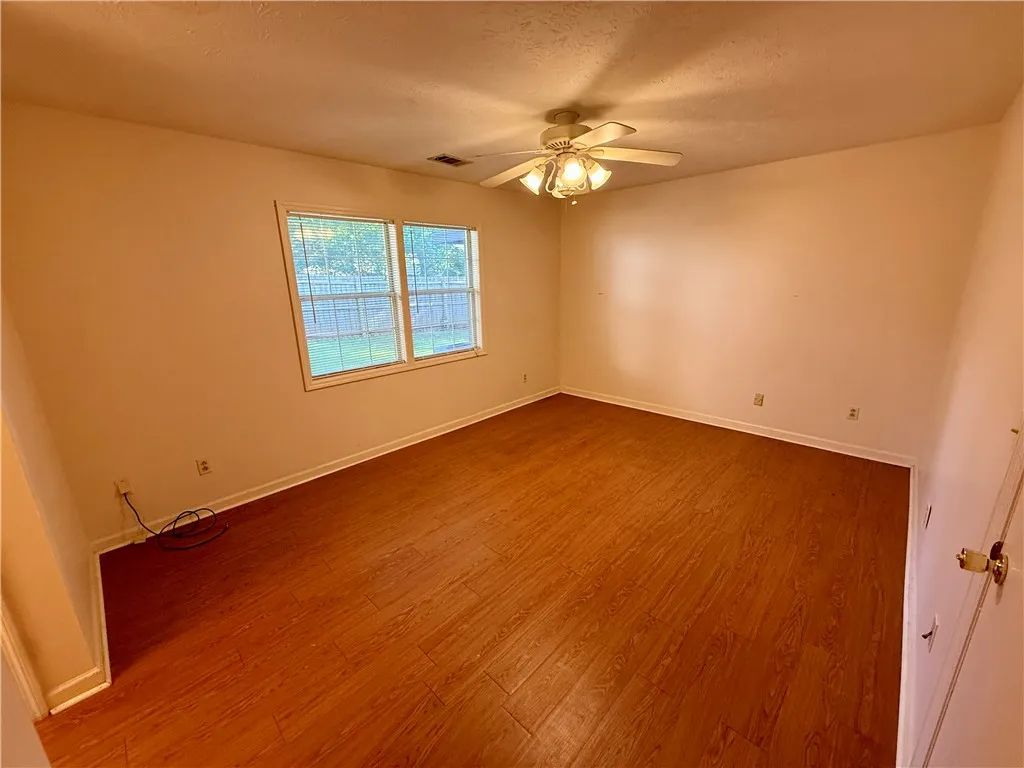 A well-lit bedroom features durable laminate flooring and a ceiling fan for comfort.