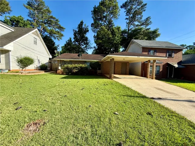A classic brick-front residence welcomes with a convenient carport and lush green landscaping.