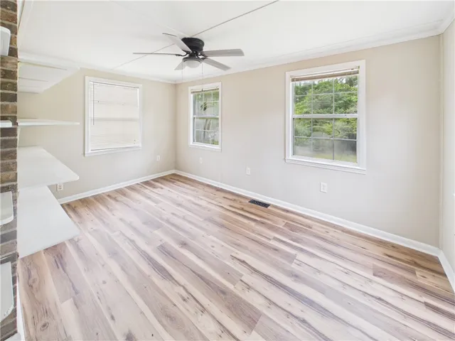 Natural light streams into this versatile room, featuring rich wood flooring and a modern ceiling fan.