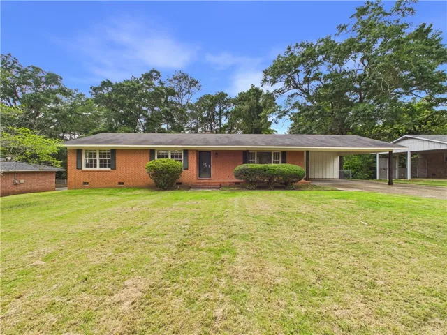 A classic brick-front home featuring a convenient carport and lush green landscaping.