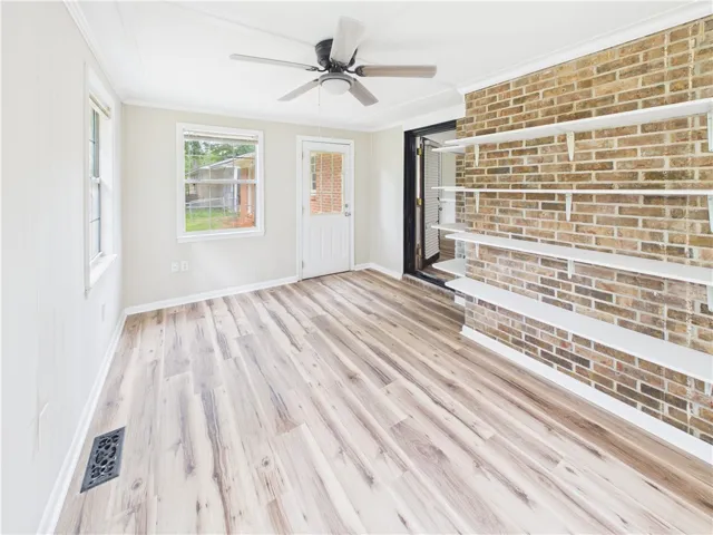 A versatile room features a striking brick accent wall with floating shelves and light wood-look flooring.