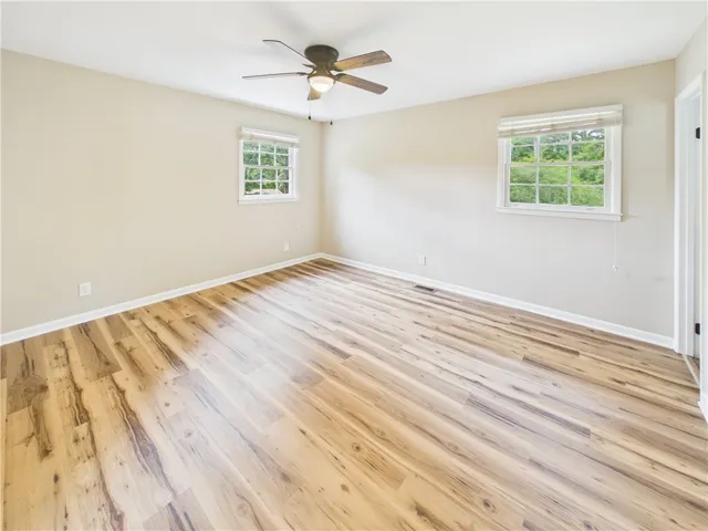 An airy bedroom offers abundant light with beautiful hardwood flooring and a ceiling fan for comfort.