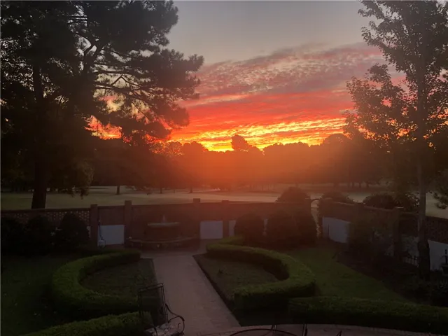 Witness vibrant skies over a tranquil landscape, featuring meticulously sculpted hedges and a charming water fountain.