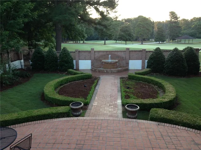 A well-manicured yard with a brick pathway leads to a tiered fountain and lush golf course beyond.