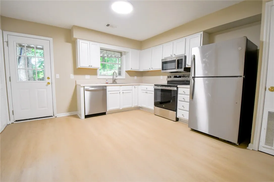 A well-equipped kitchen features light-toned flooring, white cabinetry, and a full suite of stainless steel appliances.