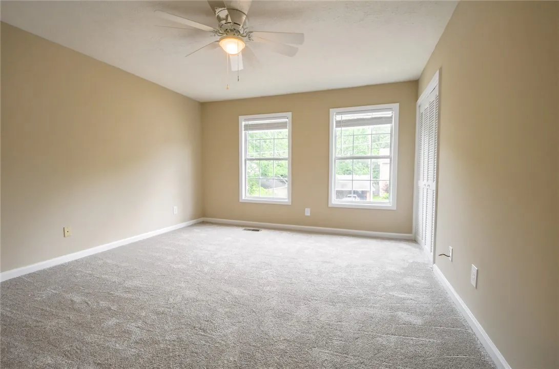 A spacious, naturally illuminated room boasts plush carpeting and a convenient ceiling fan.