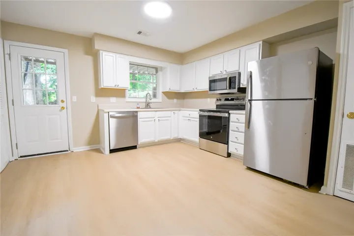 A well-equipped kitchen features light-toned flooring, white cabinetry, and a full suite of stainless steel appliances.