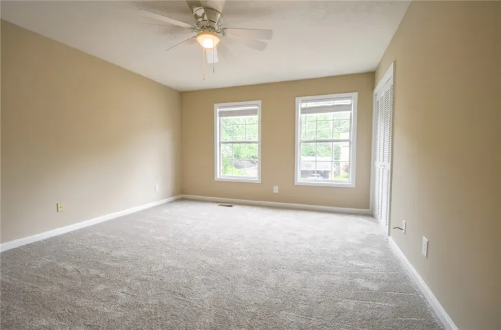 A spacious, naturally illuminated room boasts plush carpeting and a convenient ceiling fan.