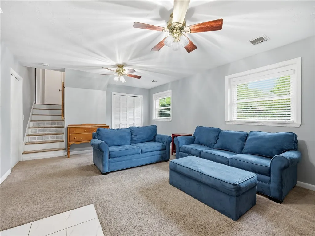 A comfortable living room features two ceiling fans and sun-filled windows, providing a refreshing atmosphere.