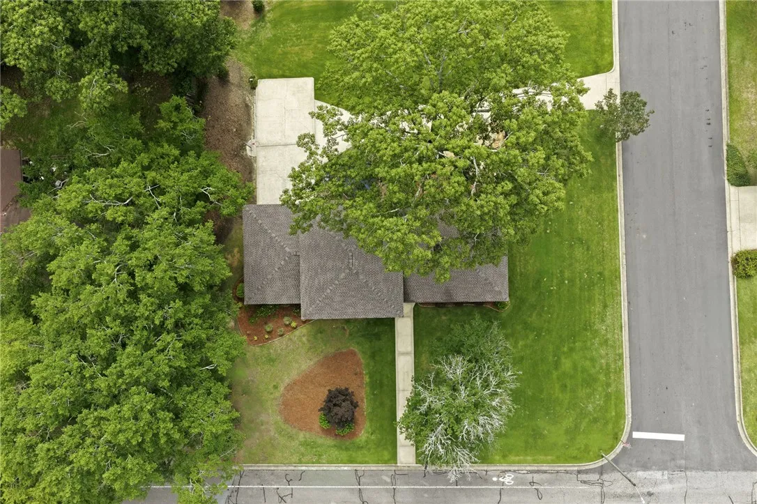 An aerial perspective showcases the verdant lot with mature trees framing the residence and paved driveways.