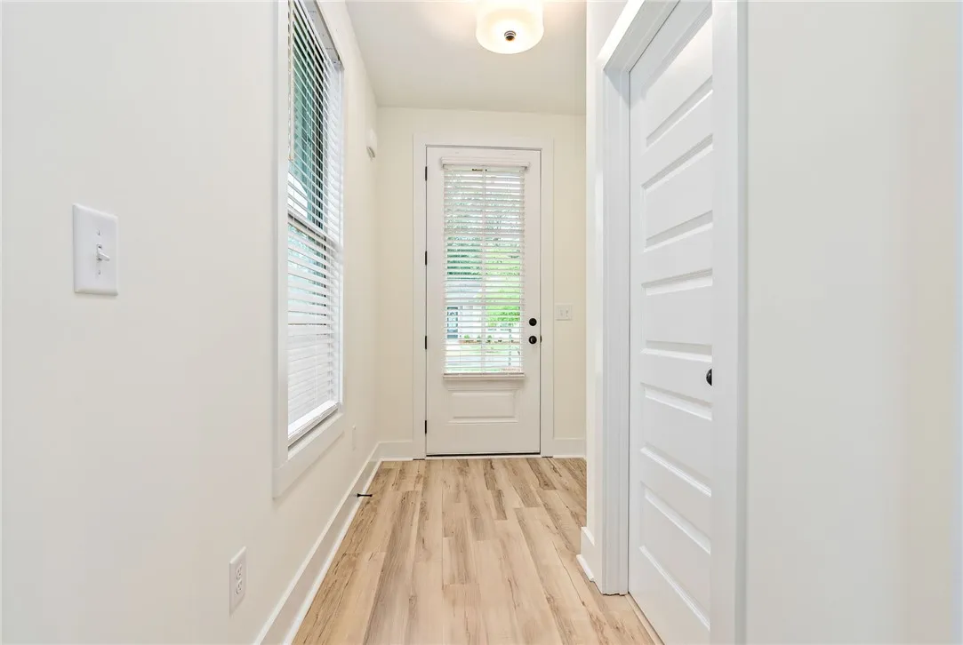 Blonde wood-look flooring extends through this well-lit entryway, leading to a paneled door with glass inserts.