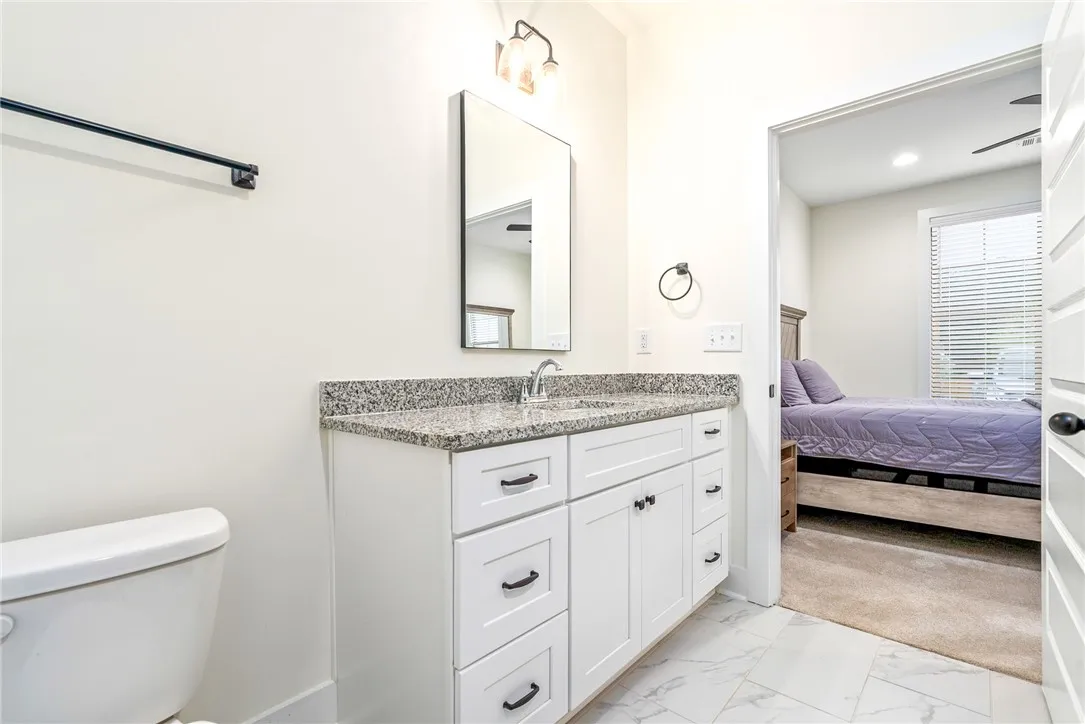 A well-appointed bath boasts granite counters and clean white cabinetry, seamlessly connecting to a cozy bedroom.
