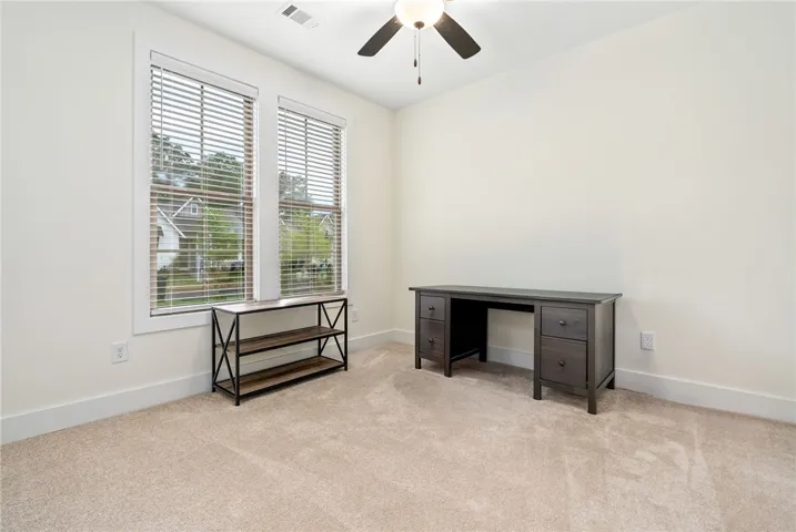 Well-lit room, perfect for a home office, with plush carpeting and two large windows offering ample natural light.