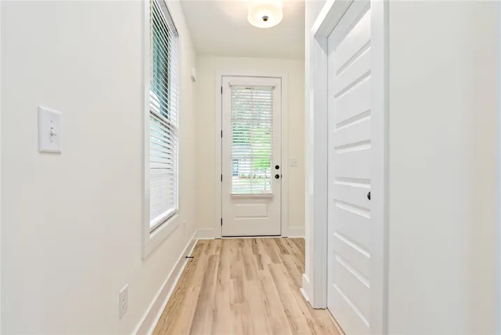 Blonde wood-look flooring extends through this well-lit entryway, leading to a paneled door with glass inserts.