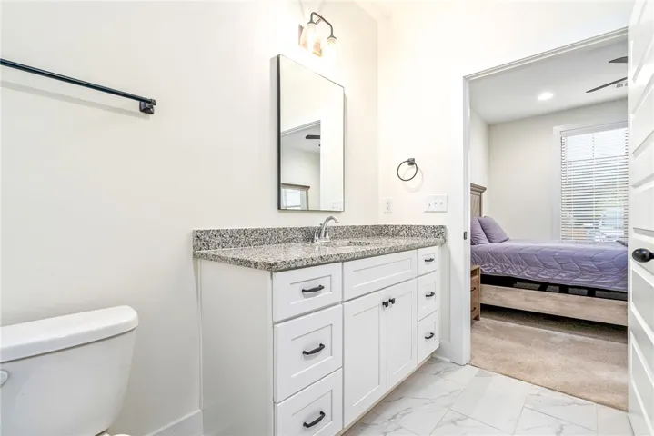 A well-appointed bath boasts granite counters and clean white cabinetry, seamlessly connecting to a cozy bedroom.