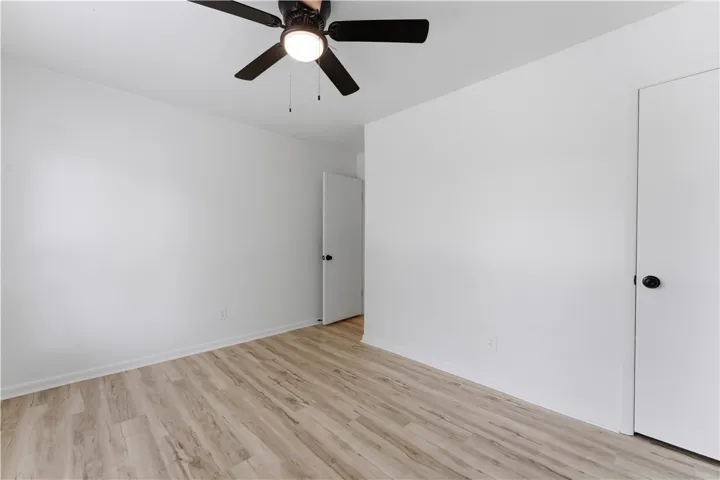A well-lit bedroom features durable laminate flooring and a ceiling fan for comfort.