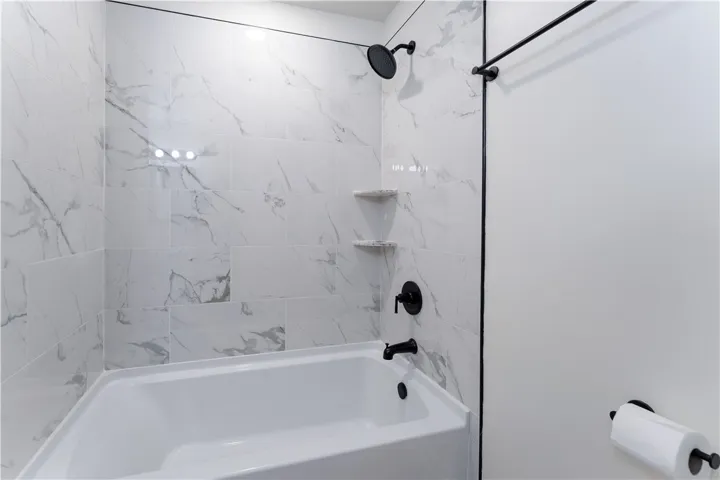 Marble-look tile surrounds this contemporary tub and shower combination with sleek dark fixtures.