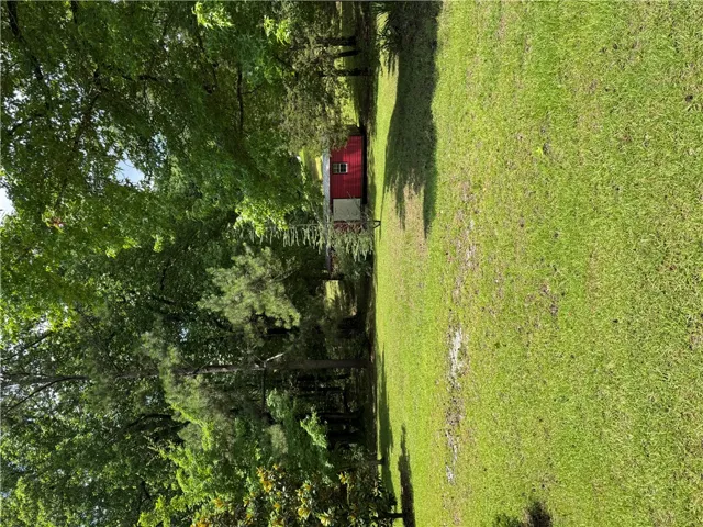 A vibrant green yard extends toward a charming red outbuilding nestled among mature trees.